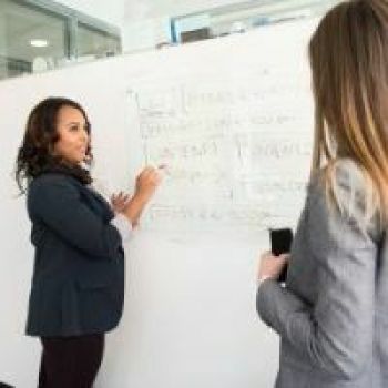 Twee personen bespreken werkinstructies aan een whiteboard